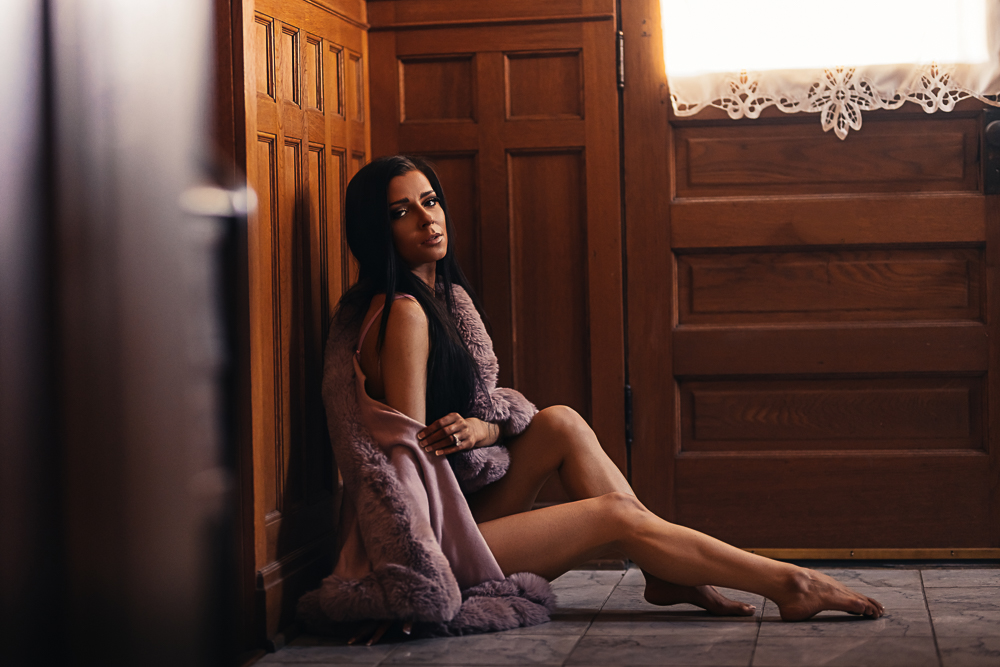Woman seated on a hardwood floor wrapped in a faux fur shawl during a St. Louis boudoir session.