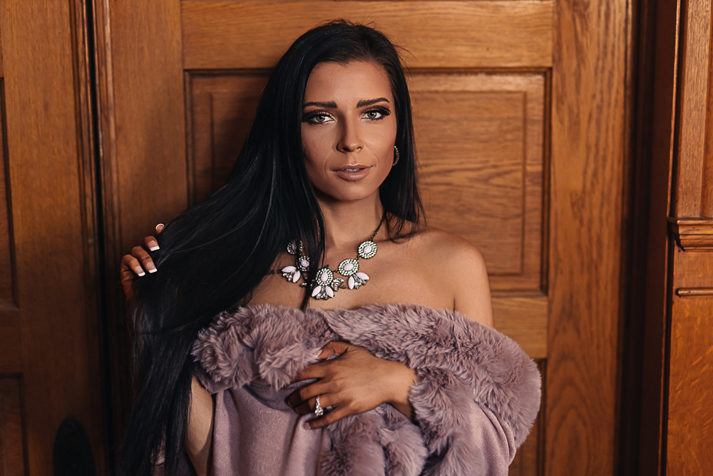 Close-up portrait of a brunette woman wrapped in a faux fur shawl wearing a floral statement necklace.