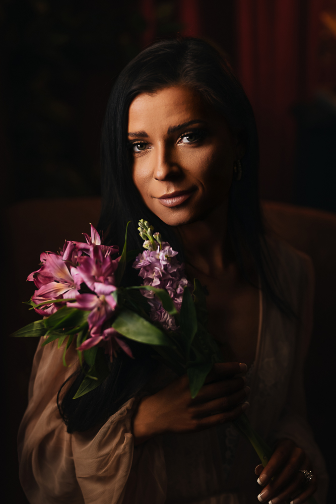 Close-up portrait of a brunette woman holding purple flowers in the Lounge during a luxury boudoir session.